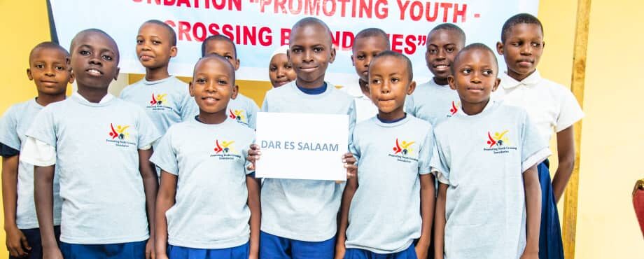 Jugendliche vor dem Stiftungsbanner, die ein Schild mit der Aufschrift Dar es Salaam hochhalten.